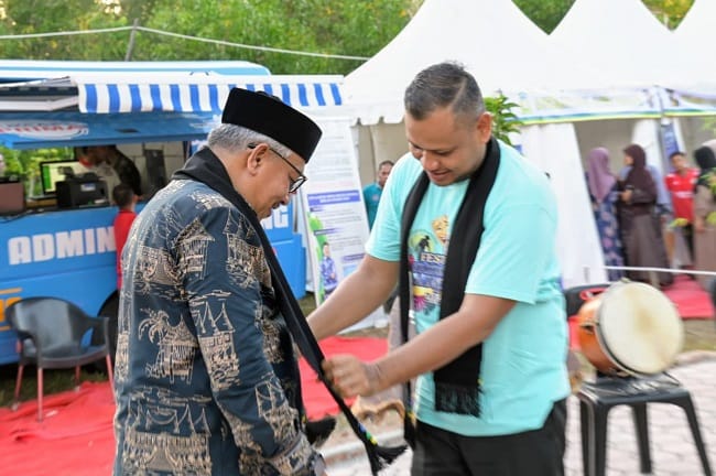 Direktur Komunitas Tikar Pandan, Yulfa memasang sal kepada Asisten 1 Sekdakab Aceh Besar Farhan AP pada acara Festifal Srimusim Lampuuk 2026 di Sekolah Adat Srimusim Lampuuk, Kecamatan Lhoknga, Aceh Besar, Kamis (30/04/2026). FOTO/MC ACEH BESAR