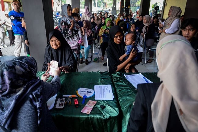 Petugas menyerahkan uang tunai kepada warga saat penyaluran bantuan sosial. Program Bantuan Sosial (Bansos) di Jawa Timur pada 2026 dipastikan tidak terdampak kebijakan pemotongan dana transfer ke daerah (TKD).(ANTARA FOTO/Putra M. Akbar)