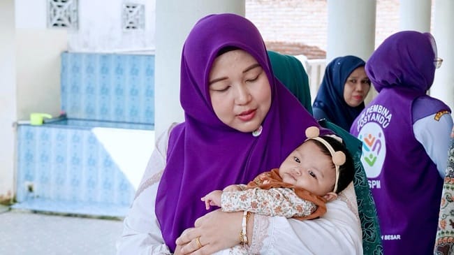 Ketua TP PKK Aceh Besar Hj. Rita Mayasari menggendong bayi saat kunjungan ke Posyandu Gampong Ajuen, Kecamatan Peukan Bada, Kamis (11/6/2026). FOTO/ MC ACEH BESAR