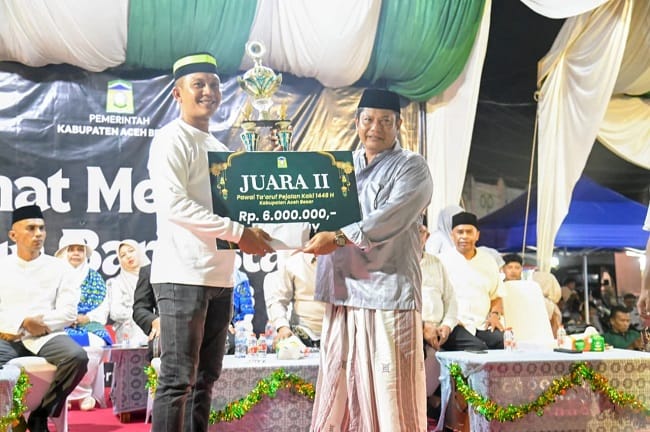 Sekdakab Aceh Besar Bahrul Jamil SSos MSi menyerahkan piala kepada juara 2 pawai pejalan kaki menyambut Tahun Baru Islam 1448 H diterima langsung oleh Azwir Ketua Pemuda Gampong Mns Papeun di depan Masjid Jamik Lambaro, Kecamatan Ingin Jaya, Aceh Besar, Senin (15/06/2026) malam. FOTO/MC ACEH BESAR
