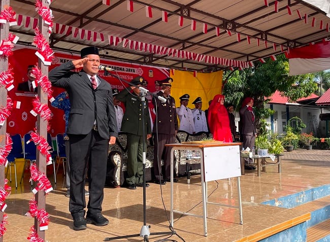Plt Camat Krueng Barona Jaya Abubakar SAg, menyerahkan bendera kepada pembawa baki, pada upacara pengibaran bendera Merah Putih, di halaman SMAN 1 Krueng Barona Jaya, Kabupaten Aceh Besar, Senin (17/8/2026). FOTO/ MC ACEH BESAR