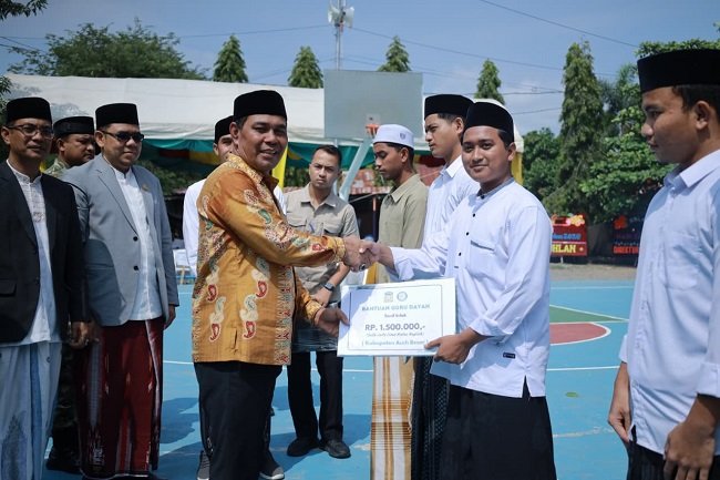 Bupati Aceh Besar H Muharram Idris (Syech Muharram) menyerahkan secara simbolis bantuan kepada guru dayah, usai upacara pengibaran bendera Merah Putih dalam rangka memperingati Hari Santri Nasional 2026, di Kompleks Dayah Ruhul Falah Anak Bangsa, Gampong Gue Gajah, Kecamatan Darul Imarah, Aceh Besar, Kamis (22/10/2026). FOTO/ PROKOPIM PEMKAB ACEH BESAR