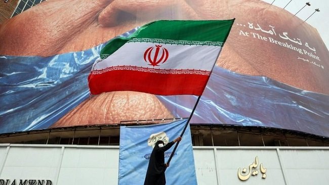 Seorang wanita melambaikan bendera Iran di depan billboard anti-AS di Alun-alun Valiasr, Teheran (dok. AFP) Seorang wanita melambaikan bendera Iran di depan billboard anti-AS di Alun-alun Valiasr, Teheran (dok. AFP)